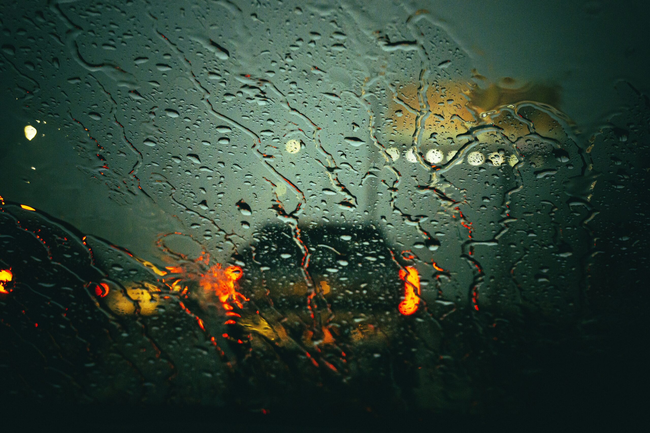 Raindrops on a car windshield reflect the red taillights of vehicles ahead, highlighting stormy weather conditions in Fort Worth, suitable for promoting storm damage tree cleanup services.